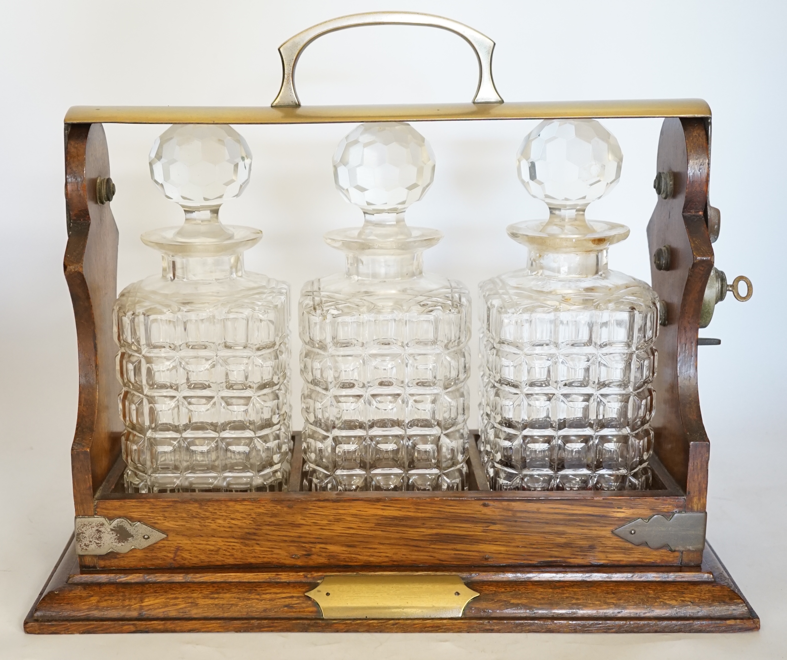 A brass mounted oak three decanter tantalus, 37cm wide. Condition - fair to good